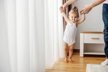 A baby girl is learning how to walk with a little help of her father.