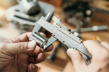 Hand of mechanic holding Vernier Caliper Measurements on a steel Shaft Bush or motorcycle part at...