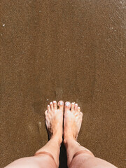 Female feet stand on the sand top view