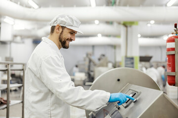 A smiling meat industry worker is pressing start button on a meat processing machine.