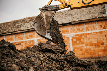 A backhoe is spilling soil on a pile on construction site.