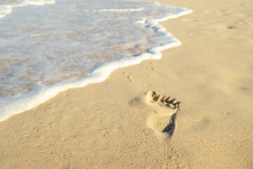 Sea waves wash away footprints of a barefoot man on a sandy beach at the water's edge. Man was walking along beach along the sea and left footprints. Concept of summer holidays, walks along the coast
