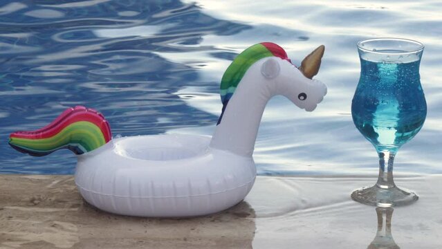 unicorn shape cup holder with pink or blue lagoon cocktail against pool.woman girl hand taking glass from ende enjoy cold refreshing beverage alcoholic.summer vacation hotel resort pool water waves 