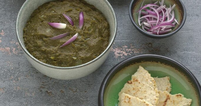 Sarson ka saag traditional Indian dish with corn bread (Makki di roti) with shallots and garlic. Homemade food meal. Table spin