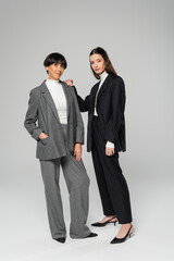 full length of asian mother and daughter in stylish pantsuits looking at camera while standing on grey background