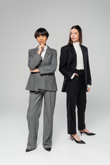 full length of middle aged asian woman with stylish daughter posing on grey background