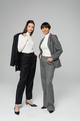 full length of asian mother and daughter in elegant attire looking at camera while posing on grey background