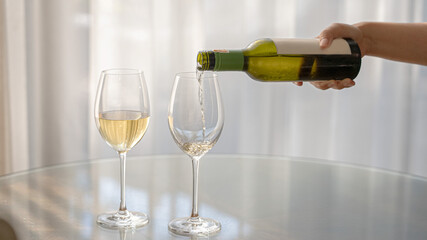 Pouring glass of white wine from a bottle. Wine tasting experience on the wooden table with couple glasses for lover honeymoon in holiday. new year cheers romantic dinner celebrate with beverage.