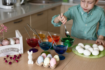 A beautiful sweet and funny red -haired boy paints eggs in the kitchen for Easter. Multi -colored eggs, the child paints at home. Close-up