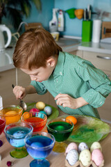 A beautiful red -haired boy paints eggs in the kitchen for Easter, at home. Close -up portrait