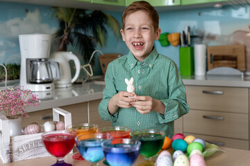 A beautiful red -haired boy paints eggs in the kitchen for Easter. Emotions laughter. Multi -colored eggs, the child paints at home. Close -up portrait