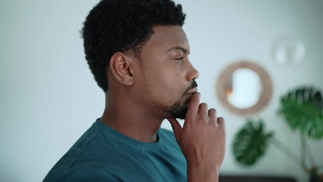 Pensive African brunet man wearing blue t-shirt thinking about something at home