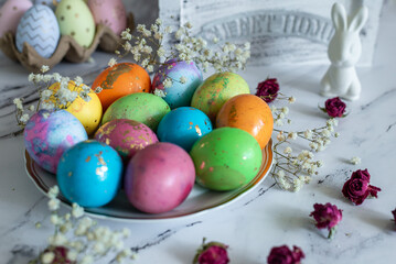 Ideas for decoration for the holiday, food composition. Beautiful multi -colored decorated Easter eggs and a cute white Easter rabbit on a white mromoic background. Close-up