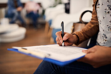 Close up of black woman writing filling medical documents in waiting room at clinic.