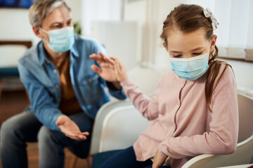 Distraught little girl and her father waiting for medical exam at doctor's office during...