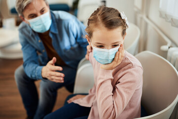  Small girl ignores her father while feeling nervous before dental exam in waiting room at dentist's office.