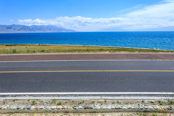 Asphalt road and lake with mountain natural scenery in Xinjiang, China.