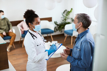 Fototapeta premium Black female doctor takes notes while communicating with patient in waiting room at clinic.