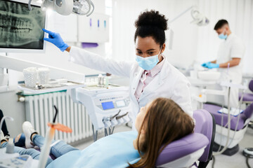 Black female dentist explains dental X-ray to teenage patient at dental clinic.