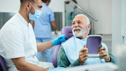 Happy senior man talks to his dentist while being satisfied with dental procedure at dentist's office.