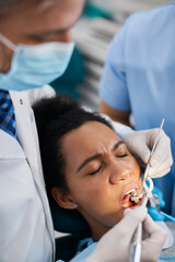 Black woman holds her eyes closed during dental procedure at dentist's office.