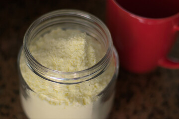 Glass container full of powdered milk along with a red cup. Natural light.