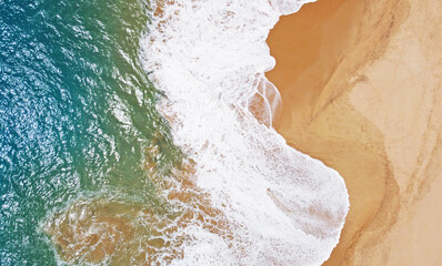 Aerial view of the waves with foam on the sandy ocean shore. Beautiful texture background for tourism and design. Tropical seashore