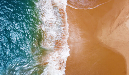 Fototapeta na wymiar Aerial view of the waves with foam on the sandy ocean shore. Beautiful texture background for tourism and design. Tropical seashore