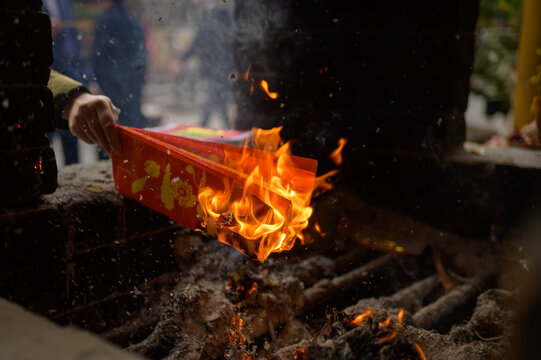 Crop unrecognizable person burning red votive paper on bonfire on street of Hoi An in Vietnam
