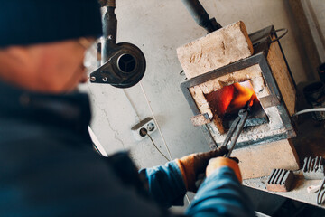 Blacksmith forge oven with hot flame. Smith put in and heating iron piece of steel in fire of red...