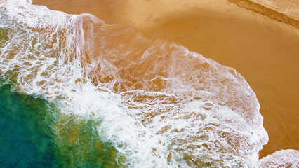 Aerial view of the waves with foam on the sandy ocean shore. Beautiful texture background for tourism and design. Tropical seashore