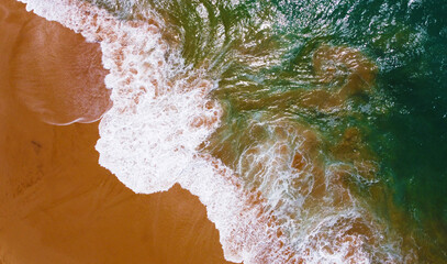 Aerial view of the waves with foam on the sandy ocean shore. Beautiful texture background for tourism and design. Tropical seashore