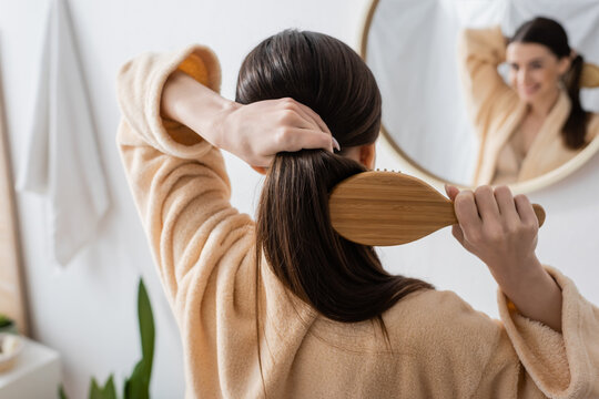 back view of young brunette woman brushing hair in bathroom.
