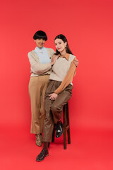 full length of young asian woman sitting on high chair near mother on coral background