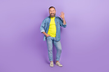 Full body photo of attractive grandpa waving hand meet friend hello wear trendy jeans garment isolated on yellow color background © deagreez