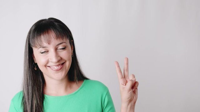 Latin American common woman wearing green blouse doing V, victory sign, with finger while smiling and looking at camera. Real people concept