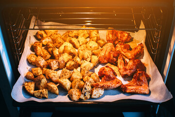 Potato and chicken with spices is baking in electric oven.