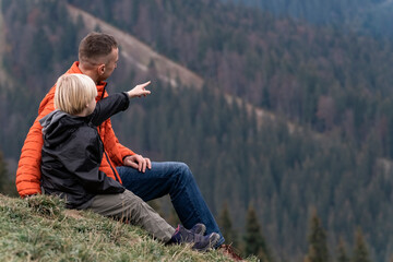 Young father and son child boy sit on slope and look at the mountains. Family hike with children in autumn.
