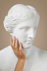 Venus sculpture with human woman's hand on beige background