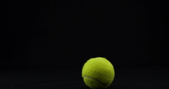 Green tennis ball bouncing isolated on black background. The tennis ball hits and bounces beautifully against the black background. A round tennis ball jumps on a black table.