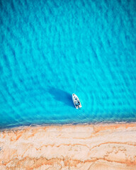 White yacht and turquoise water waves from top view. Beach with yellow sand glowing by sunlight. Travel summer vacations seascape background from drone