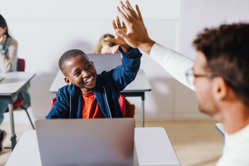 Teacher and student doing a high five in a computer science classroom, celebrating a successful...