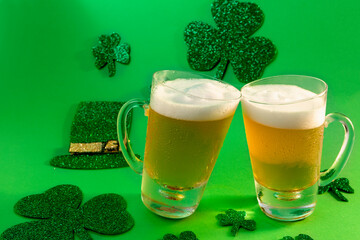 Two mugs of cold beer on green background with shamrock and hat, st patrick's day