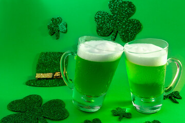 Two mugs of cold green beer on green background with shamrock and hat, st patrick's day
