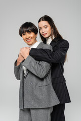 cheerful asian mother and daughter in stylish blazers looking at camera isolated on grey