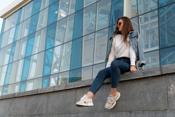 Attractive stylish woman resting on city street. Young woman in sunglesses in youth clothing on the city street