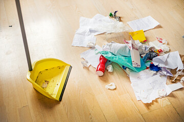 teenage girl cleans up the trash in her room with a shovel on the parquet,