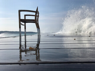Chaise en bois sur une jetée avec une grosse vague en arrière plan