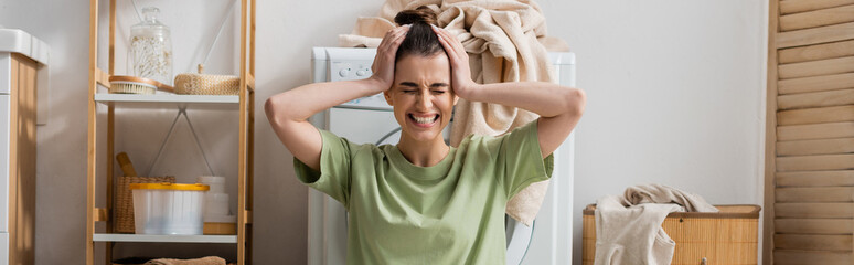 tensed woman touching head near washing machine in laundry room, banner.