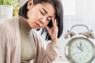 Asian woman suffering from chronic daily headache with alarm clock in foreground